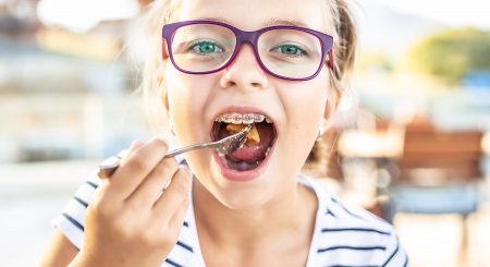 Young girl wearing glasses and braces puts food on fork into her mouth.